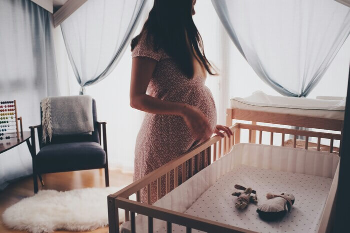 Une femme enceinte à côté d'un berceau dans la chambre de son bébé à venir